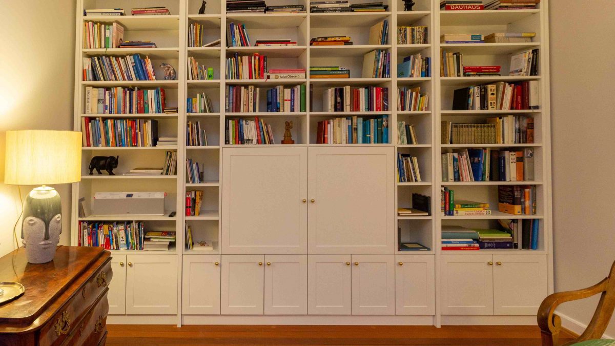 Bücherregal, weiß lackiert, mit geschlossenen Fächern unten und Türen vor dem Fernsehgerät. Geplant und hergestellt von der Schreinerei Freymark in Freiburg
