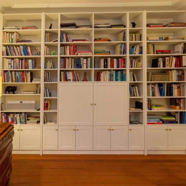 B&uuml;cherregal, wei&szlig; lackiert, mit geschlossenen F&auml;chern unten und T&uuml;ren vor dem Fernsehger&auml;t. Geplant und hergestellt von der Schreinerei Freymark in Freiburg