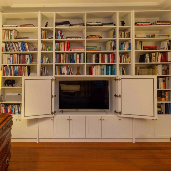 B&uuml;cherregal, wei&szlig; lackiert, mit geschlossenen F&auml;chern unten und ge&ouml;ffneten T&uuml;ren mit sichtbarem Fernsehger&auml;t. Geplant und hergestellt von der Schreinerei Freymark in Freiburg