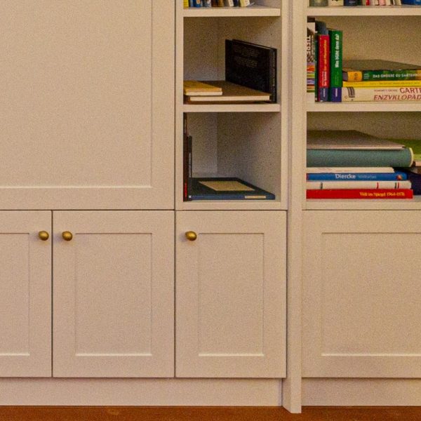 B&uuml;cherregal, wei&szlig; lackiert, mit geschlossenen F&auml;chern unten und T&uuml;ren vor dem Fernsehger&auml;t. Geplant und hergestellt von der Schreinerei Freymark in Freiburg