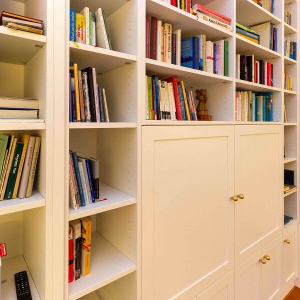 B&uuml;cherregal, wei&szlig; lackiert, mit geschlossenen F&auml;chern unten und T&uuml;ren vor dem Fernsehger&auml;t. Geplant und hergestellt von der Schreinerei Freymark in Freiburg