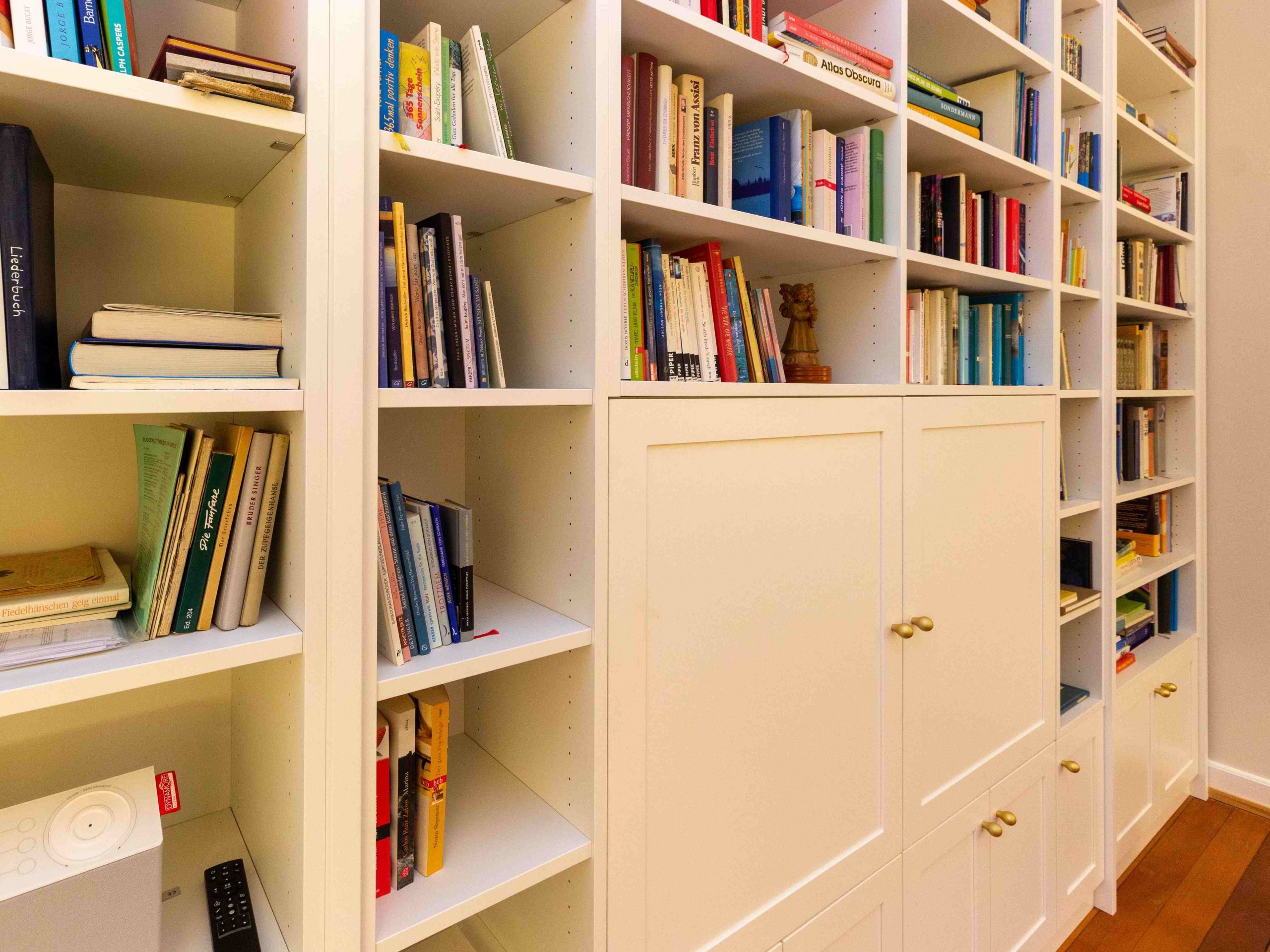 B&uuml;cherregal, wei&szlig; lackiert, mit geschlossenen F&auml;chern unten und T&uuml;ren vor dem Fernsehger&auml;t. Geplant und hergestellt von der Schreinerei Freymark in Freiburg