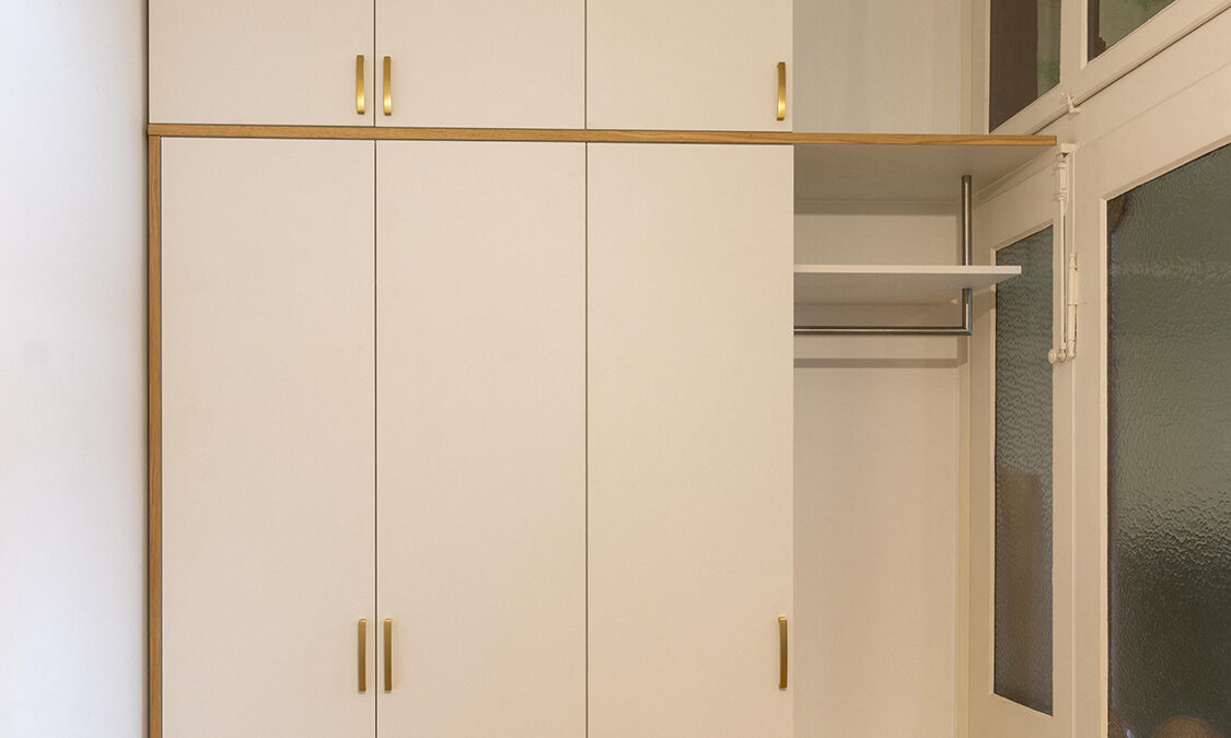 Garderobenschrank im Altbau mit weißen Fronten, Messinggriffen und Akzenten in Eiche