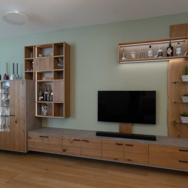 Schreinerm&ouml;bel in Eiche, schwarzen Griffen, Beton-Optik und variabler LED-Beleuchtung vor salbeigr&uuml;n gestrichener Wand