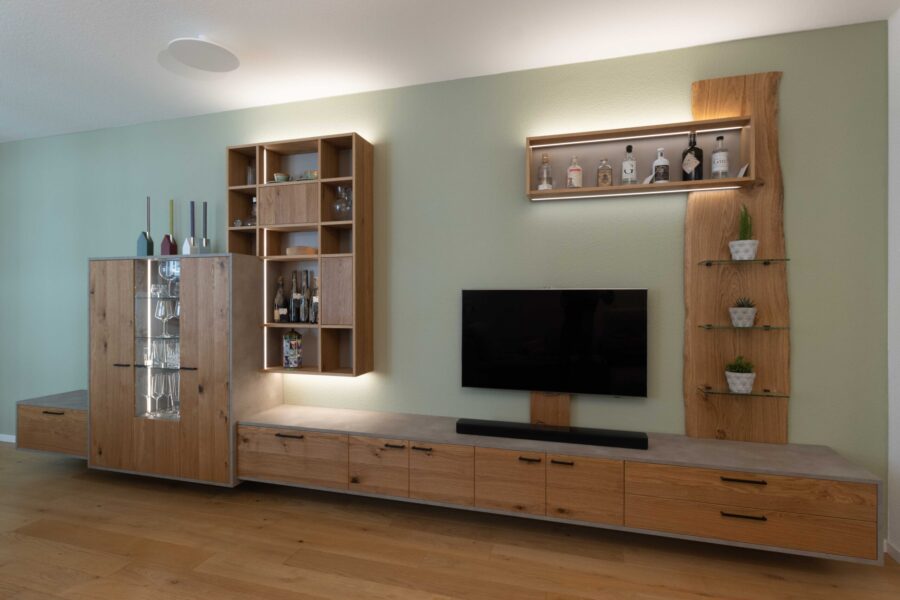 Wohnzimmer vom Schreiner: Schreinerm&ouml;bel in Eiche, schwarzen Griffen, Beton-Optik und variabler LED-Beleuchtung vor salbeigr&uuml;n gestrichener Wand